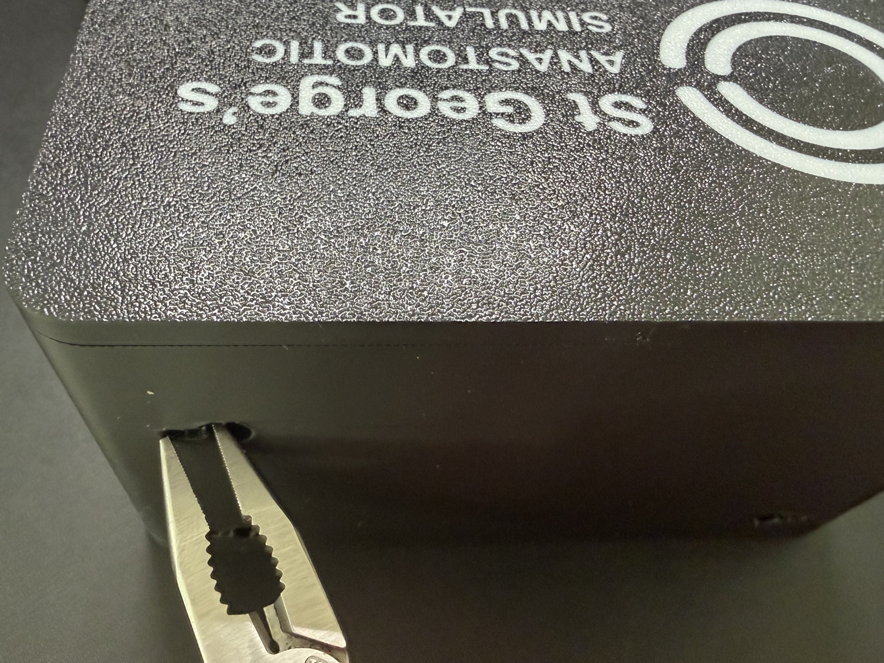 Pliers clearing print support from a suction-cup keyhole hanger on the simulator case.